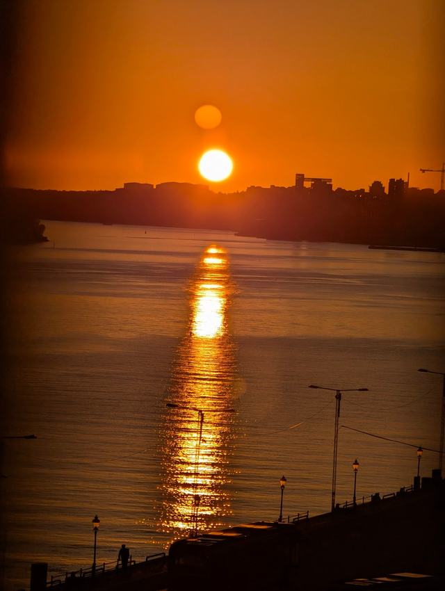 An orange sun low over dark water, with a second, fainter reflection of the sun just above it and a golden path of light across the water.